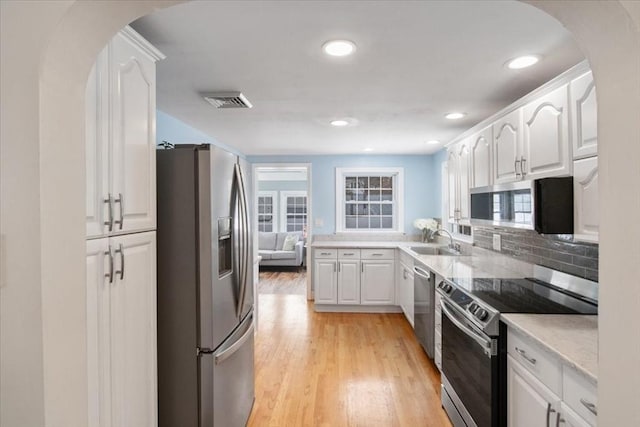 kitchen featuring arched walkways, white cabinetry, light wood finished floors, and stainless steel appliances