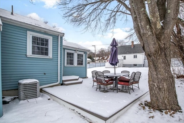 snow covered patio featuring central air condition unit, outdoor dining space, and fence