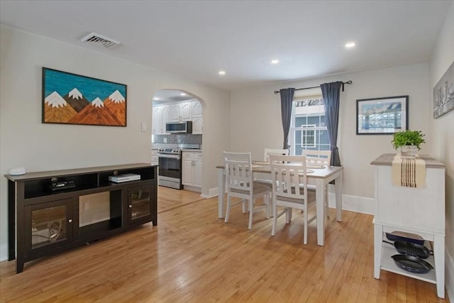 dining space with light wood finished floors, visible vents, baseboards, recessed lighting, and arched walkways