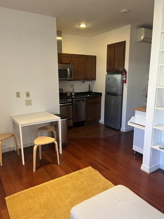 kitchen featuring baseboards, a wall unit AC, stainless steel appliances, and dark wood-style floors