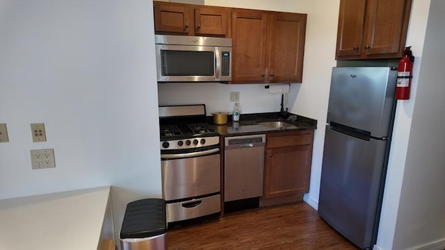 kitchen with dark wood-style flooring, baseboards, dark stone counters, brown cabinets, and stainless steel appliances