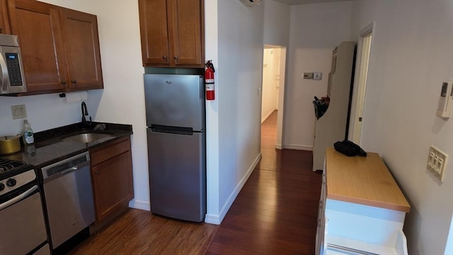 kitchen featuring baseboards, dark stone counters, a sink, dark wood finished floors, and stainless steel appliances