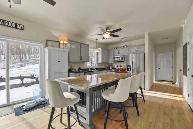 kitchen featuring gray cabinets, ceiling fan, stainless steel appliances, light stone counters, and a kitchen island