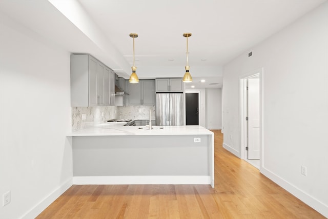 kitchen with hanging light fixtures, kitchen peninsula, gray cabinetry, stainless steel refrigerator, and light hardwood / wood-style floors