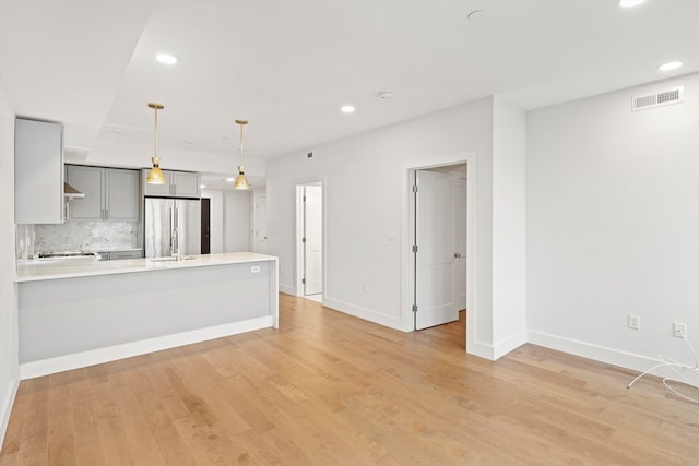 kitchen with gray cabinetry, stainless steel refrigerator, kitchen peninsula, light wood-type flooring, and decorative light fixtures