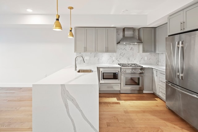 kitchen featuring light hardwood / wood-style floors, wall chimney exhaust hood, kitchen peninsula, stainless steel appliances, and sink