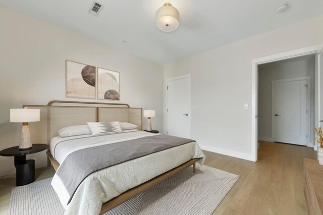 bedroom with baseboards, visible vents, and wood finished floors
