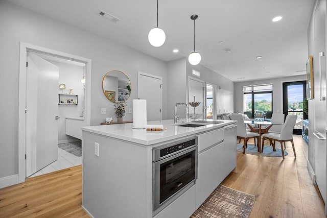 191 Washington St Unit 308, Boston, MA 02135 - kitchen featuring white cabinets, open floor plan, decorative light fixtures, a kitchen island with sink, and light wood finished floors