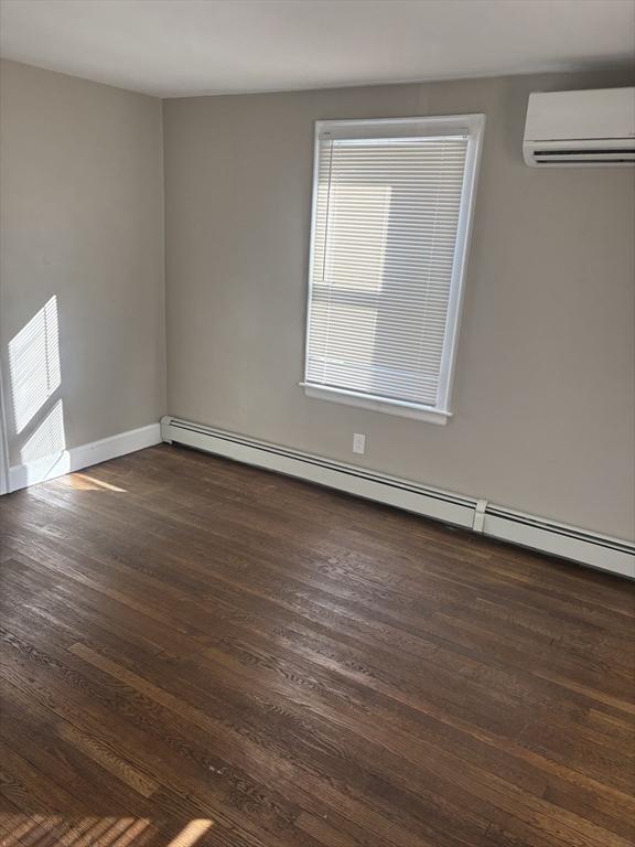 unfurnished room with a wall mounted air conditioner, a baseboard radiator, and dark wood-type flooring