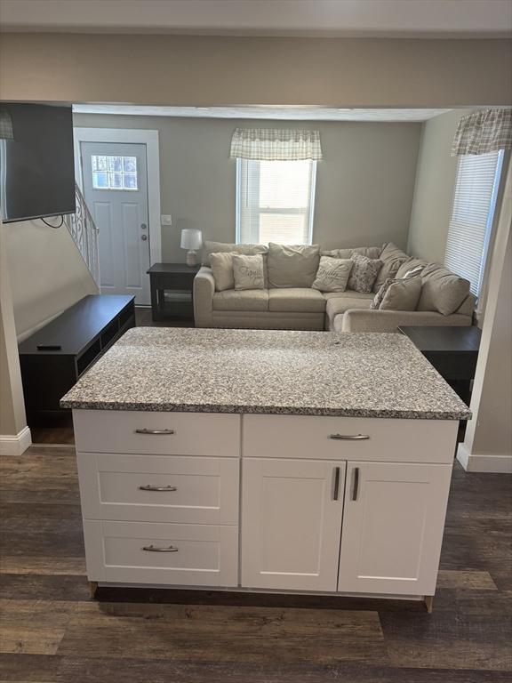 kitchen featuring white cabinetry, dark hardwood / wood-style flooring, a kitchen island, and light stone counters