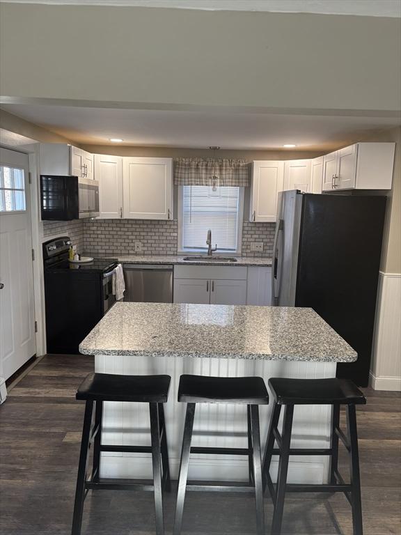 kitchen with white cabinets, a kitchen island, stainless steel appliances, and a breakfast bar area