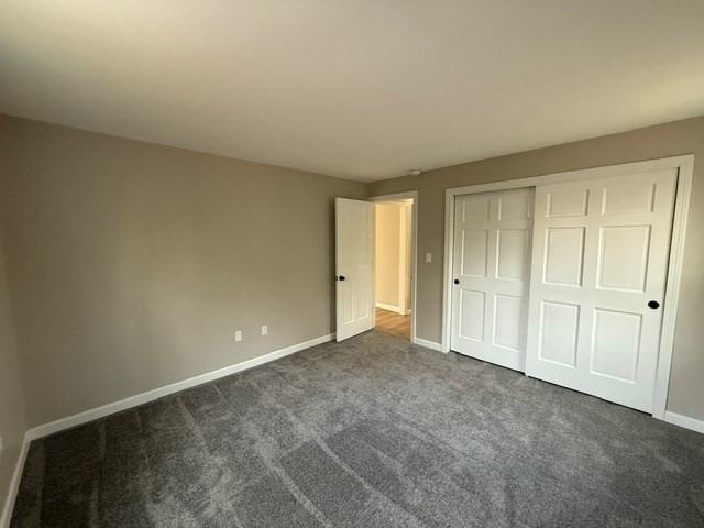 unfurnished bedroom with dark carpet and a closet