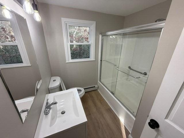 full bathroom with hardwood / wood-style floors, bath / shower combo with glass door, vanity, a baseboard radiator, and toilet