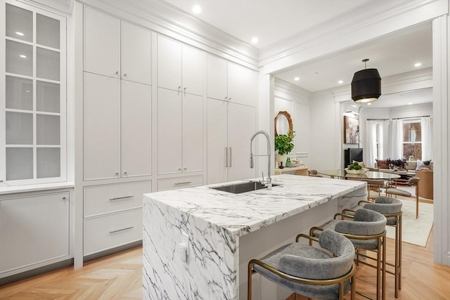 kitchen with an island with sink, sink, white cabinets, light parquet floors, and ornamental molding