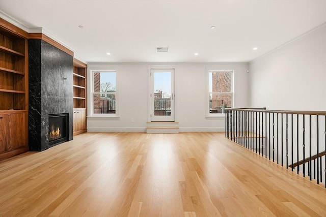 unfurnished living room featuring built in shelves, a fireplace, and light hardwood / wood-style flooring