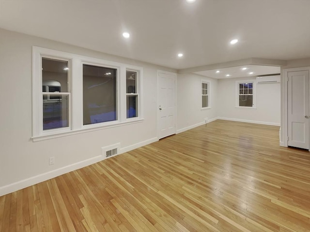 spare room featuring a wall unit AC, light wood-style flooring, baseboards, and visible vents