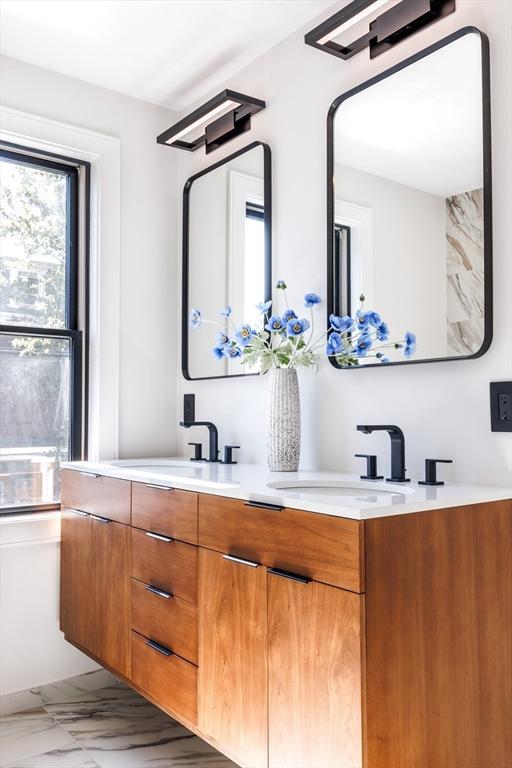 full bath with marble finish floor, double vanity, and a sink