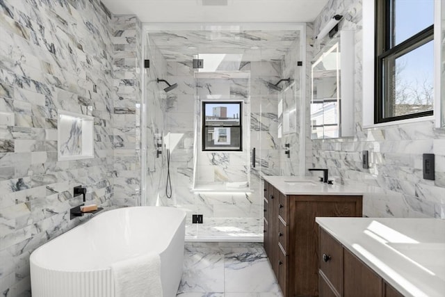 full bath with marble finish floor, tile walls, a marble finish shower, vanity, and a freestanding tub