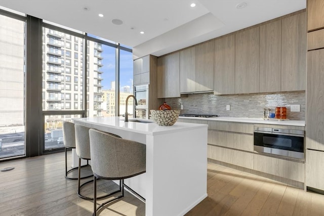 kitchen with a city view, light countertops, an island with sink, modern cabinets, and a wall of windows