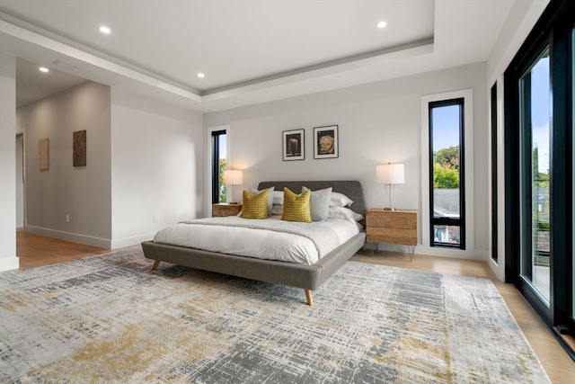 bedroom featuring a raised ceiling, access to exterior, and light hardwood / wood-style flooring