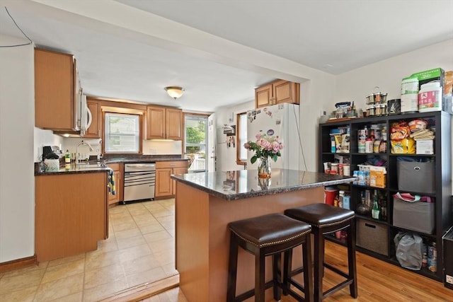 82 Brickel Rd, Stoughton, MA 02072 - kitchen with white appliances, a kitchen island, a breakfast bar area, a sink, and dark stone countertops