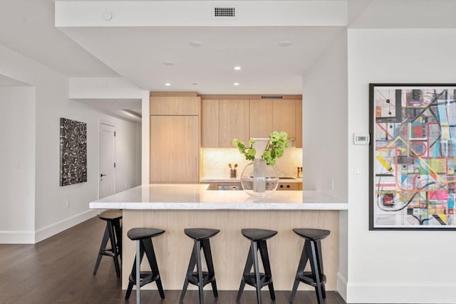 kitchen with light brown cabinets, visible vents, a kitchen breakfast bar, light stone countertops, and dark wood-style floors