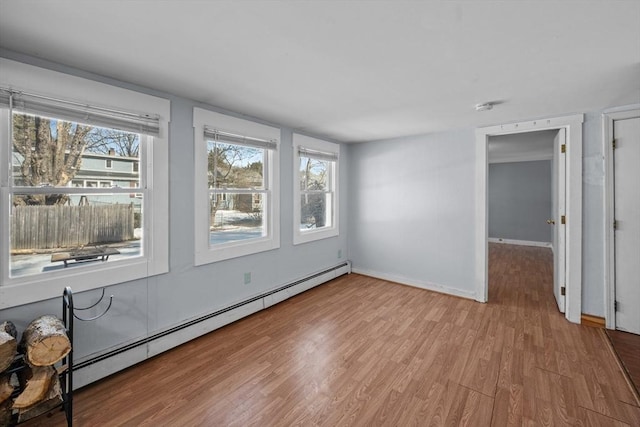 empty room with a baseboard heating unit, baseboards, and light wood finished floors