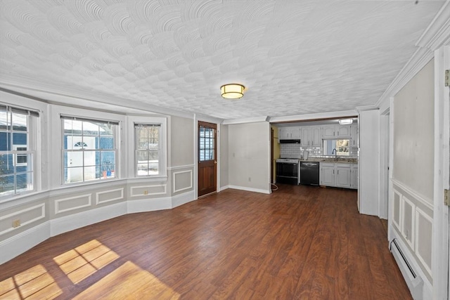 unfurnished living room featuring a sink, baseboard heating, a healthy amount of sunlight, and dark wood-style floors