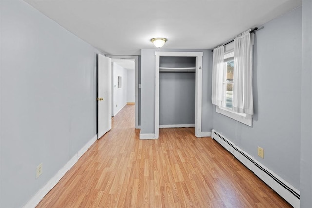 unfurnished bedroom featuring a closet, baseboards, baseboard heating, and light wood finished floors