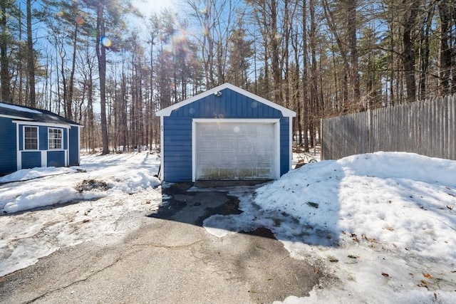 snow covered garage featuring driveway, a detached garage, and fence