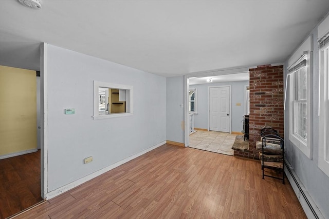 interior space featuring a baseboard heating unit, wood finished floors, baseboards, and a healthy amount of sunlight