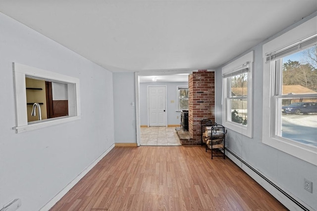 unfurnished room with baseboard heating, light wood-type flooring, and baseboards