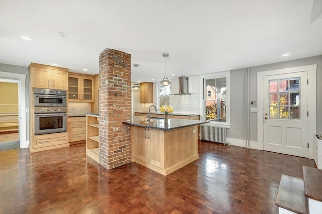 kitchen featuring radiator heating unit, wall chimney range hood, double oven, decorative light fixtures, and decorative backsplash