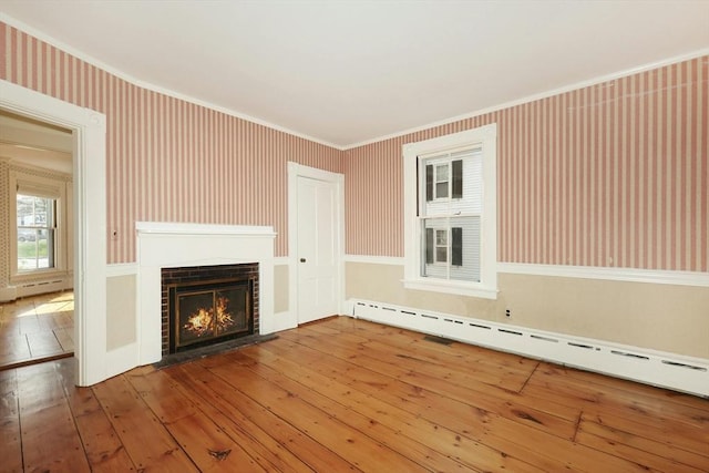 unfurnished living room featuring wood-type flooring, crown molding, and a baseboard heating unit