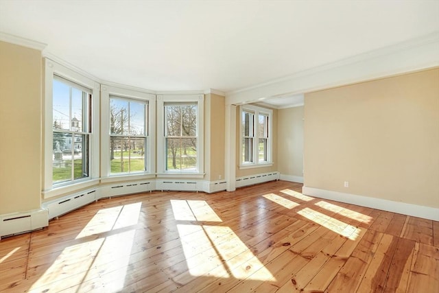 empty room featuring baseboard heating, light hardwood / wood-style flooring, and ornamental molding