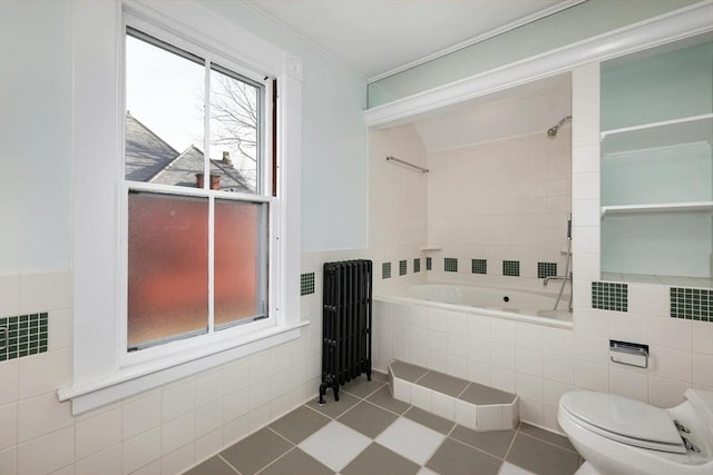 bathroom featuring radiator, tile patterned flooring, tiled bath, toilet, and tile walls