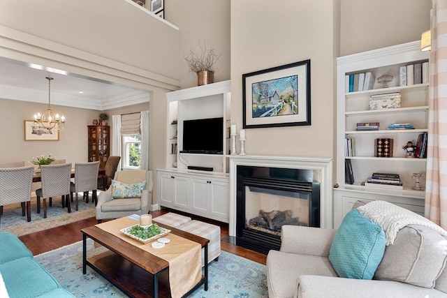 living room featuring built in features, a glass covered fireplace, wood finished floors, and a notable chandelier