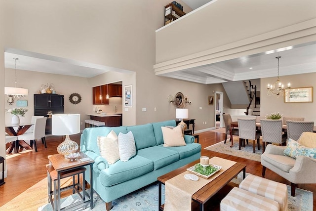living room featuring light wood-type flooring, stairs, baseboards, and a notable chandelier