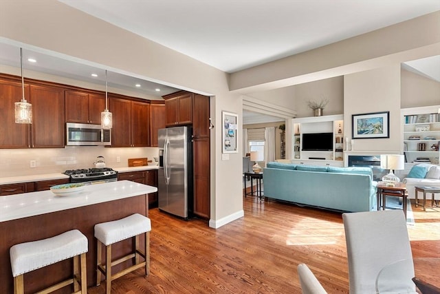 kitchen with wood finished floors, a breakfast bar area, light countertops, appliances with stainless steel finishes, and hanging light fixtures