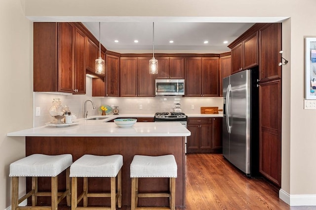 kitchen with appliances with stainless steel finishes, a breakfast bar, a sink, a peninsula, and wood finished floors