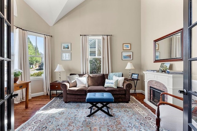 living area with baseboards, a glass covered fireplace, wood finished floors, and high vaulted ceiling