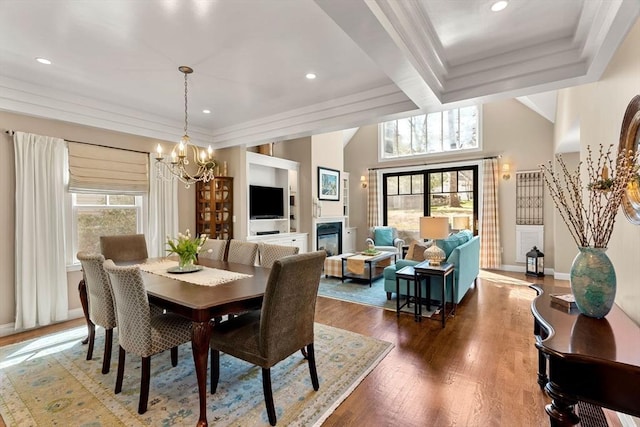 dining space with an inviting chandelier, a glass covered fireplace, crown molding, and wood finished floors