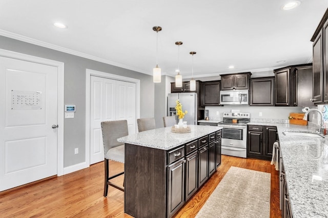 kitchen with stainless steel appliances, light hardwood / wood-style floors, sink, hanging light fixtures, and a kitchen island