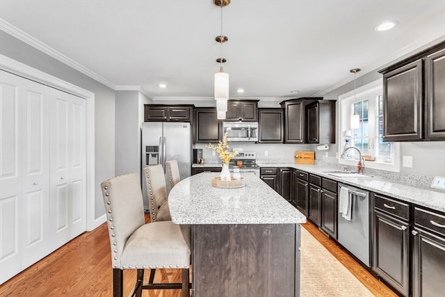 kitchen featuring sink, appliances with stainless steel finishes, decorative light fixtures, a center island, and light wood-type flooring