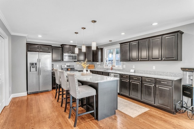 kitchen with stainless steel appliances, a kitchen breakfast bar, hanging light fixtures, light hardwood / wood-style flooring, and a center island