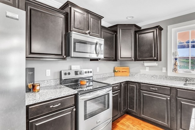 kitchen with ornamental molding, light wood-type flooring, appliances with stainless steel finishes, and light stone counters