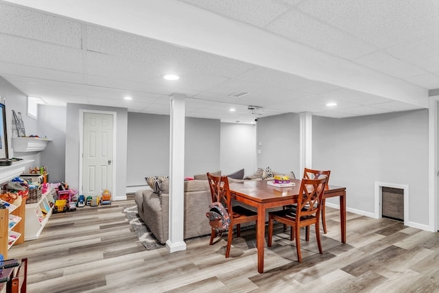 dining area with light wood-type flooring, a drop ceiling, and a baseboard radiator