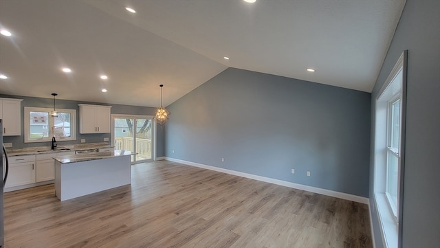 kitchen featuring white cabinetry, a center island, light hardwood / wood-style floors, decorative light fixtures, and vaulted ceiling