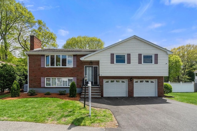 bi-level home with an attached garage, asphalt driveway, a chimney, and brick siding