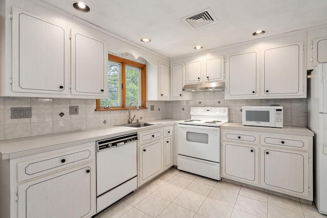 kitchen featuring white appliances, under cabinet range hood, light countertops, decorative backsplash, and a sink